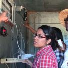 three women looking at man's arm pointing to air conditioner and CoolBot controller